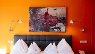 Bett im Deluxe Zimmer Seeblick im Boutiquehotel Cortisen am Wolfgangsee mit modernem Kunstwerk an der Wand und stilvoller Einrichtung