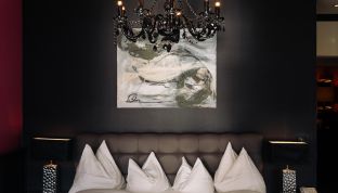 Bett der Black Suite im Boutiquehotel Cortisen am Wolfgangsee mit elegantem Kronleuchter und stilvollem Designambiente