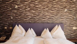 Bett im Deluxe Zimmer Seeblick im Boutiquehotel Cortisen am Wolfgangsee mit auffälliger Designtapete und modernem Interieur