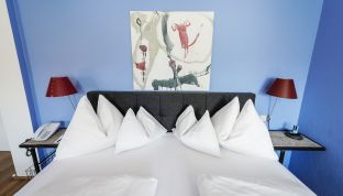 Kunstgemälde hinter einem Bett an der Wand in der Loft Suite im Designhotel Cortisen am Wolfgangsee