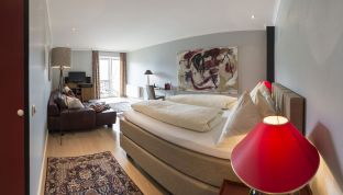 Zimmer der Red Suite mit Doppelbett, Sitzecke und Kunst im Designhotel Cortisen am Wolfgangsee