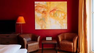 Kunstwerk und stilvoller Sessel im Deluxe Zimmer Seeblick im Boutiquehotel Cortisen am Wolfgangsee mit hochwertigem Interieur und moderner Atmosphäre