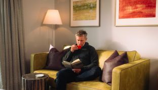 Mann trinkt Kaffee und liest ein Buch auf einer Couch im Adults Only Boutique Hotel Cortisen am Wolfgangsee