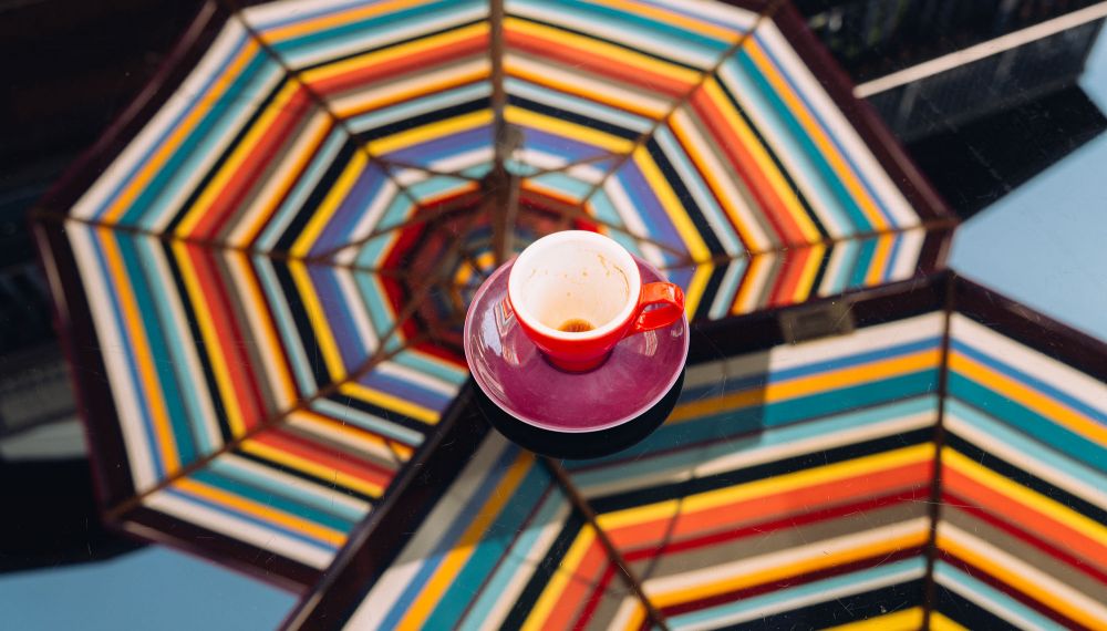 leere Kaffeetasse auf einem Tisch mit der Spiegelung von Sonnenschirmen im Adults Only Hotel Cortisen am Wolfgangsee