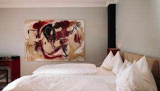 Bett der Red Suite Design Suite im Boutiquehotel Cortisen am Wolfgangsee mit modernem Kunstwerk an der Wand und stilvollem Interieur