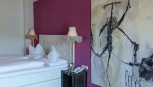 Doppelbett und Kunstgemälde im White Suite Design Zimmer im Arthotel Cortisen am Wolfgangsee im Salzkammergut